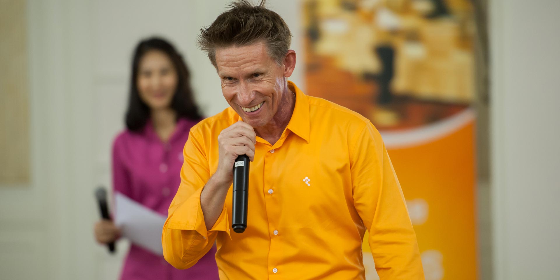 Facilitator in an orange shirt speaking into a microphone at the UNICEF workshop