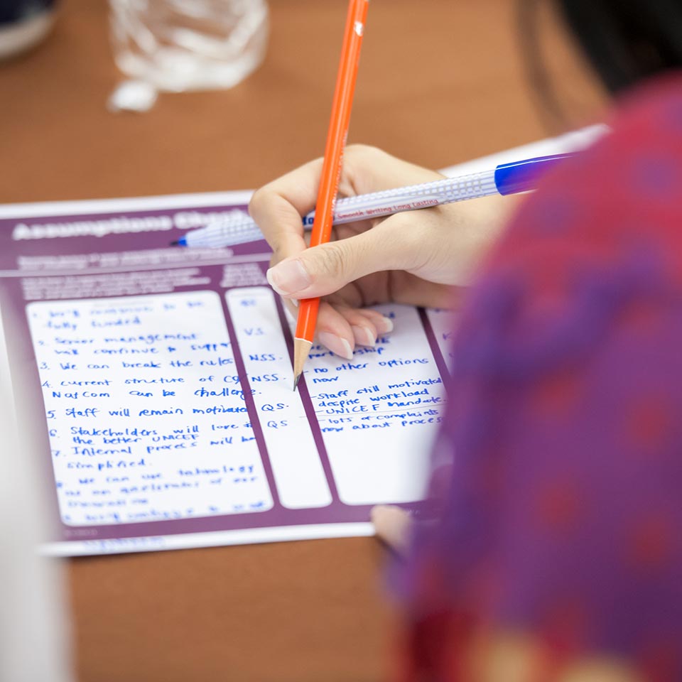 Participant filling in an assumptions sheet with coloured pens, UNICEF project
