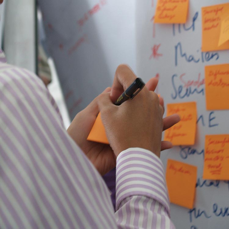 Participant writing on an orange sticky note in front of an ideas board, Mead Johnson project