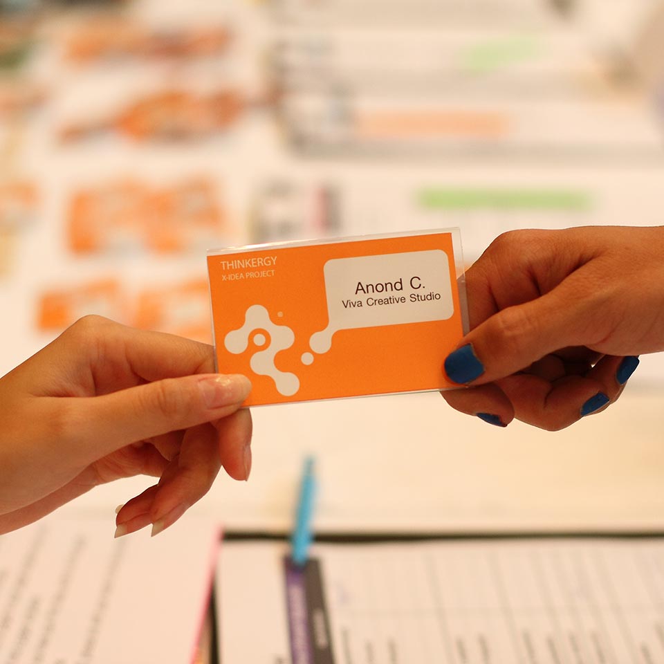 Hands exchanging an orange Thinkergy name card at the Nestle workshop