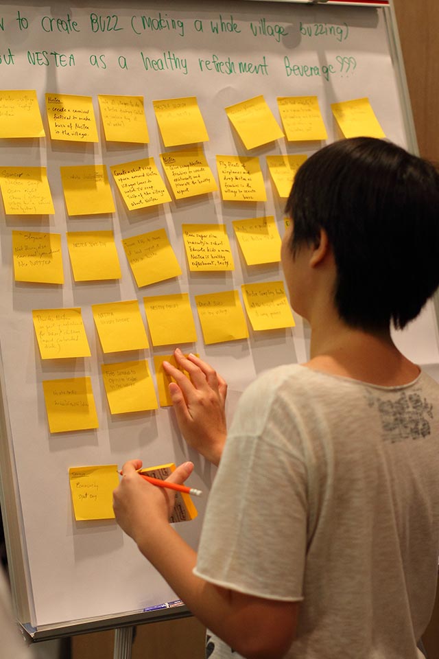 Participant arranging yellow sticky notes on a whiteboard, Nestle project