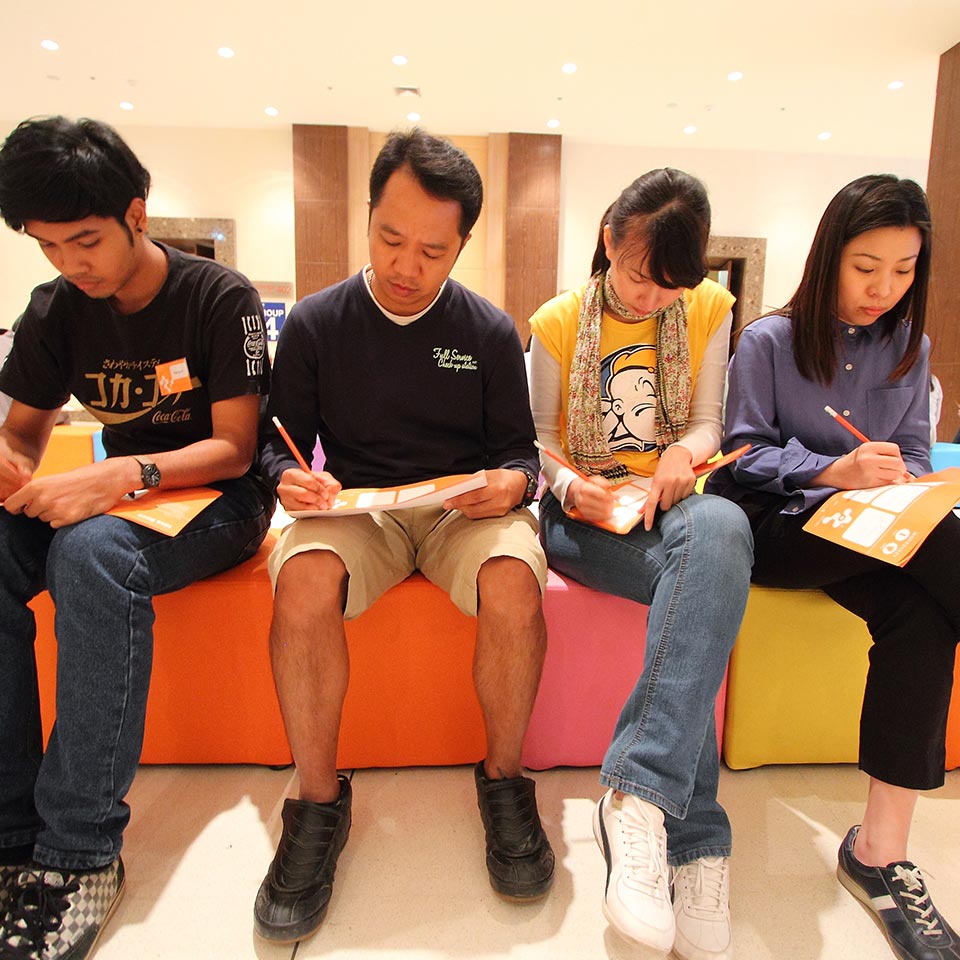 Four Nestle participants on colourful benches writing on orange worksheets