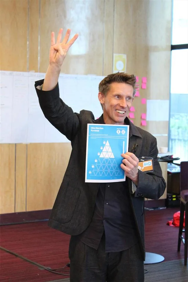 Facilitator raising a hand and holding an X-IDEA worksheet, Sandbox Global workshop