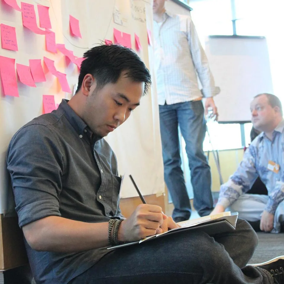 Participant sketching ideas on a clipboard while seated on the floor, Sandbox Global