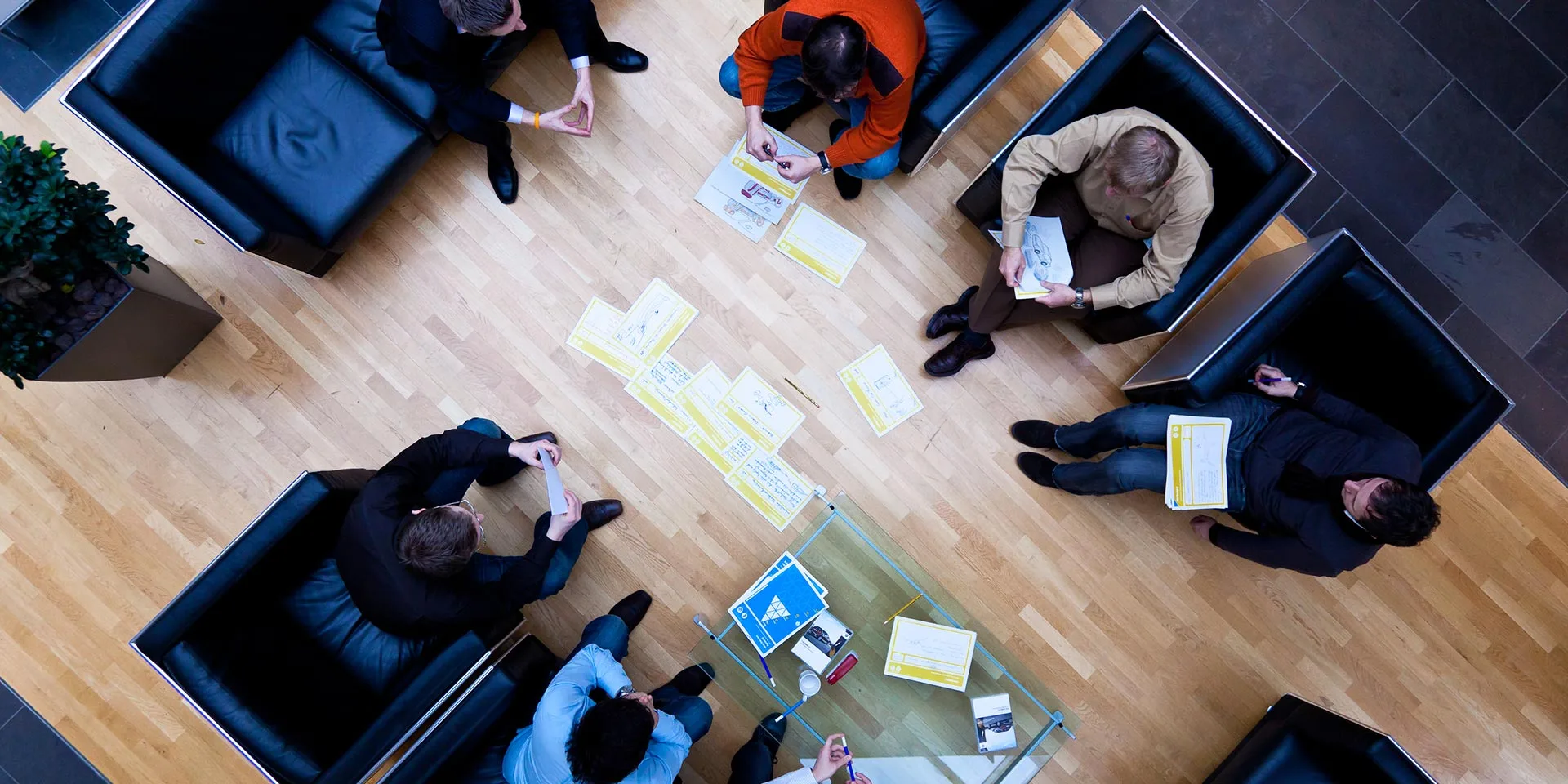 Overhead view of BMW workshop participants in armchairs around a table of worksheets