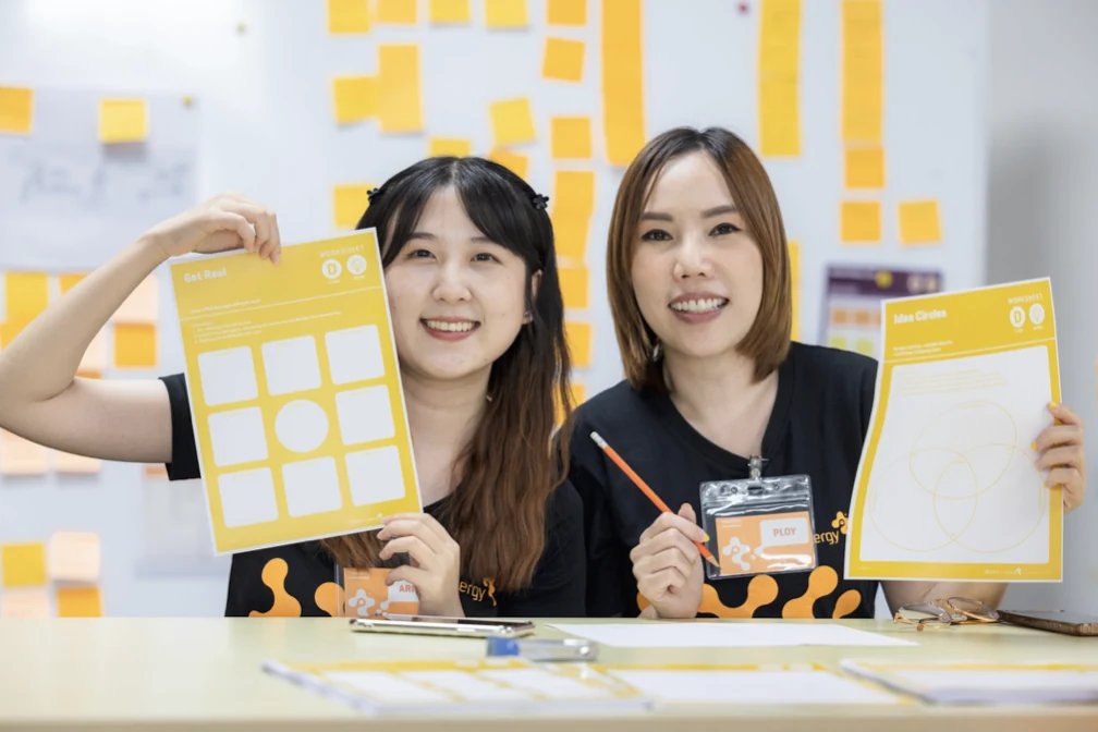 Two Continental team members holding up their worksheets in front of an idea wall