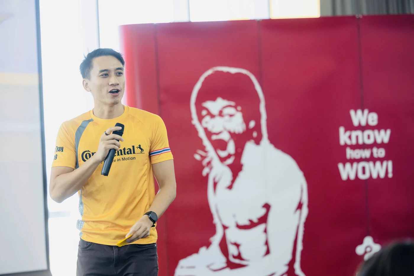 A Continental trainee presenting with a microphone in front of the We know how to WOW banner