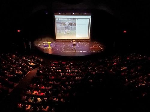 Kevin speaking to a large crowd from a large semi-circular stage.