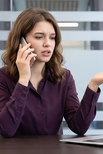 Aggravated woman on phone while looking at laptop