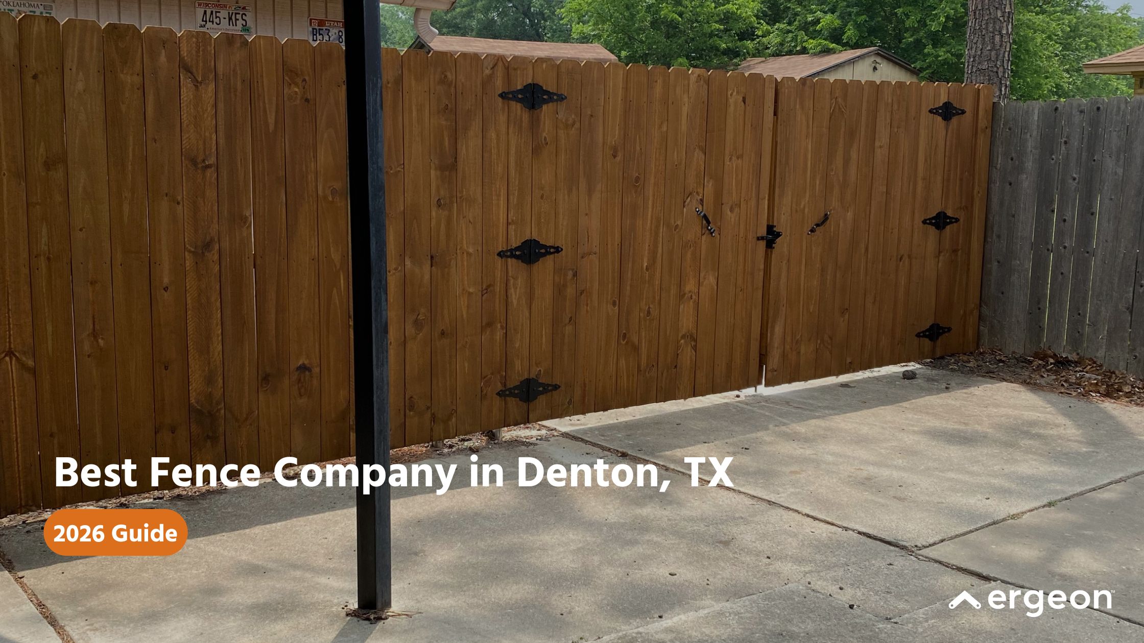 Wooden Fence and Gate Installation in Denton, TX - 2026 Guide This image features a newly installed wooden privacy fence and gate on a concrete surface in a residential setting. The fence consists of vertical wooden planks with black metal hinges and hardware for the gate. Various license plates are mounted on the structure behind the fence, indicating a personal or decorative touch. The photograph is used in a 2026 guide promoting the best fence company services in Denton, Texas, highlighting quality fence craftsmanship suitable for residential properties.