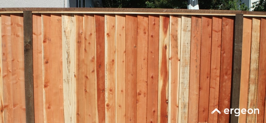 Close-up View of a Wooden Fence Panel Installed in San Jose This image shows a close-up view of a newly installed wooden fence panel. The fence is constructed with vertical wooden planks in varying shades of natural wood, supported by a horizontal wooden beam at the top. The fence appears to be sturdy and freshly installed, suitable for residential property boundaries or garden enclosures. The natural wood finish and visible grain highlight the quality and craftsmanship of the installation.