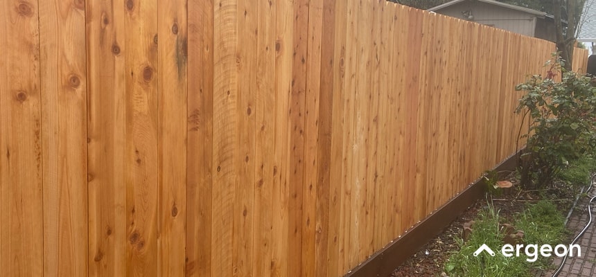 Durable Cedar Wood Fence Suitable for Seattle Weather This image shows a long, well-constructed cedar wood fence featuring vertical wooden planks with a smooth finish. The fence is installed outdoors along a garden bed, demonstrating its suitability for residential use. The cedar wood is known for its natural resistance to moisture, decay, and insects, making it an ideal choice for the damp and rainy climate typical of Seattle. The fence appears sturdy and well-maintained, indicating its potential for providing privacy, security, and weather resilience in similar environments.