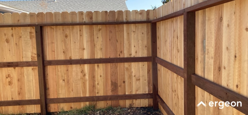 This image shows a freshly installed wooden privacy fence corner section featuring vertical cedar planks supported by horizontal and vertical dark-stained wooden braces. The construction style is designed to withstand the weather conditions typical in areas like Tacoma, Washington. The fence panels are closely spaced for privacy and stability, making it suitable for residential backyards looking for durable and aesthetically pleasing boundary solutions.