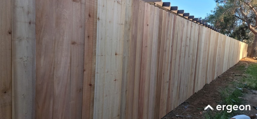 Cedar Privacy Fence Installation for Temecula Residential Homes This image depicts a newly installed wooden privacy fence made of cedar panels along the perimeter of a residential property. The fence features vertically aligned boards with a clean, natural finish, providing both aesthetic appeal and security. The setting suggests typical use in suburban homes in Temecula, emphasizing privacy and property boundary definition. The fence is shown in daylight, with clear blue skies and trees in the background, highlighting the durability and craftsmanship of the cedar material.