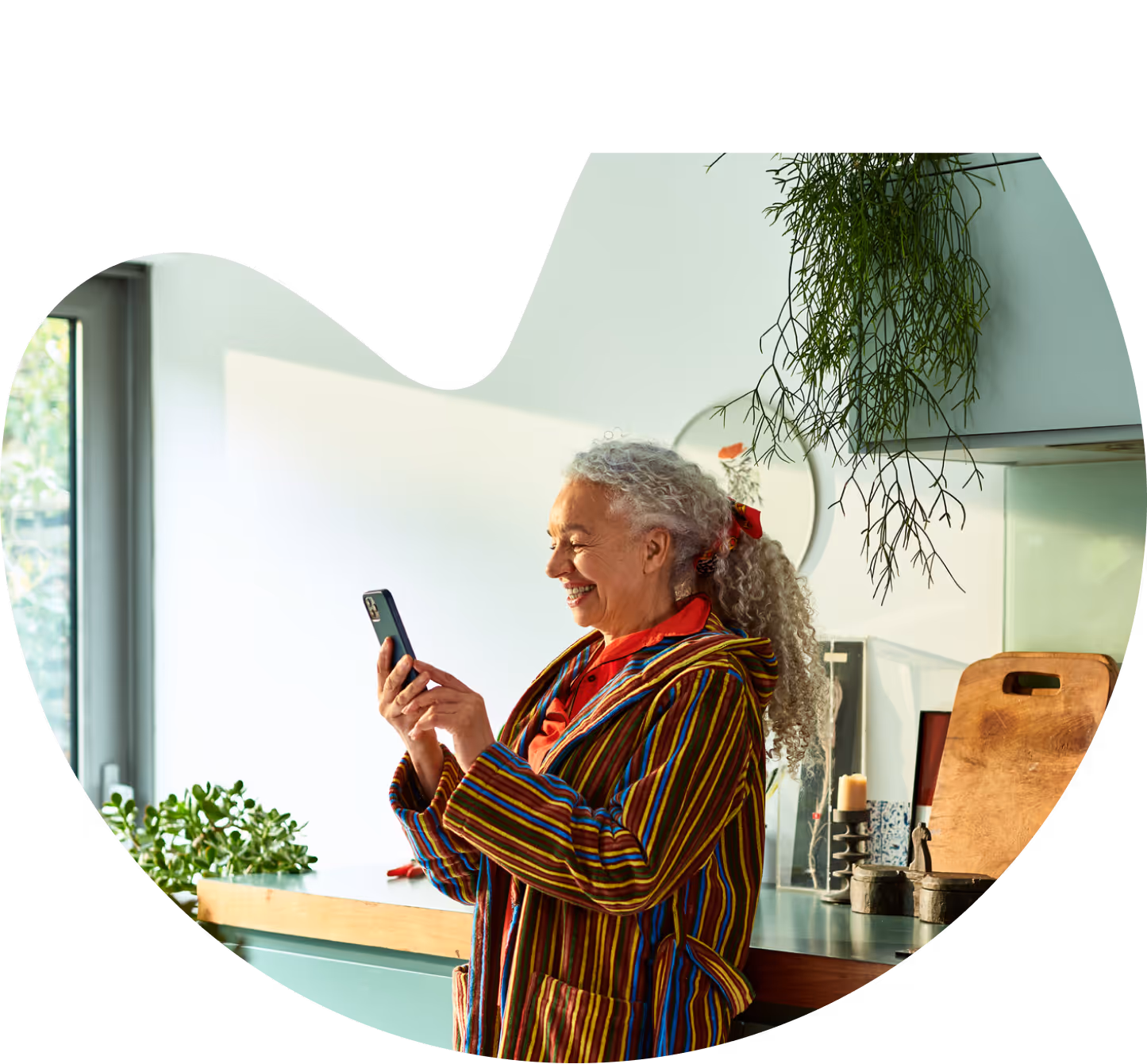 A woman, smiling, holding a phone in her kitchen.