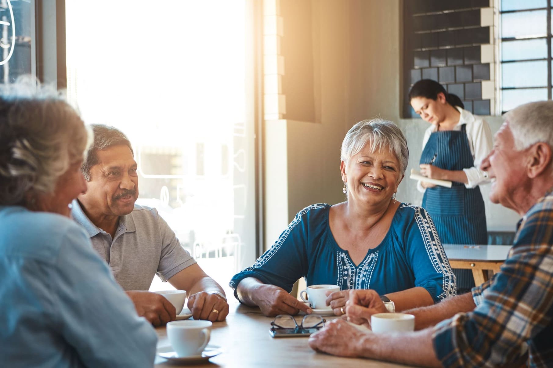 Group of smiling seniors enjoying coffee together in a bright cafe, some have dentures from Saberton via the CDCP