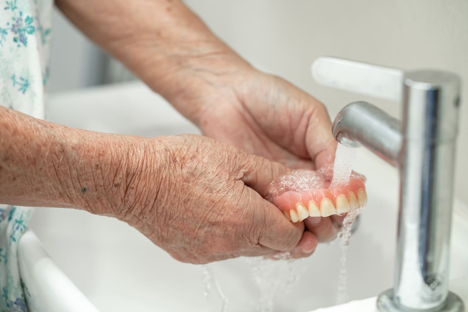 Person rinsing dentures under running water to remove cleanser and residue