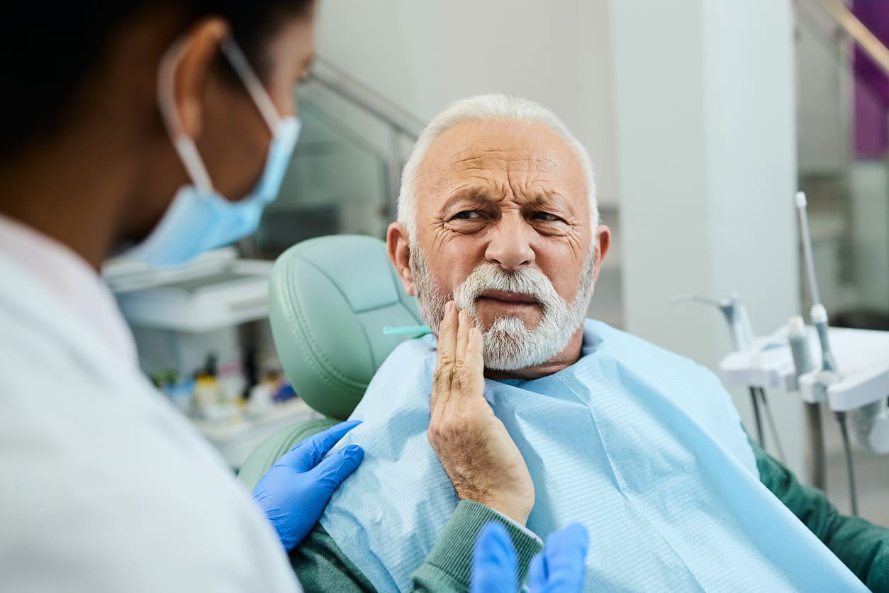 Elderly man in dental chair with denturist examining denture fit issues and discussing treatment options for sore spots