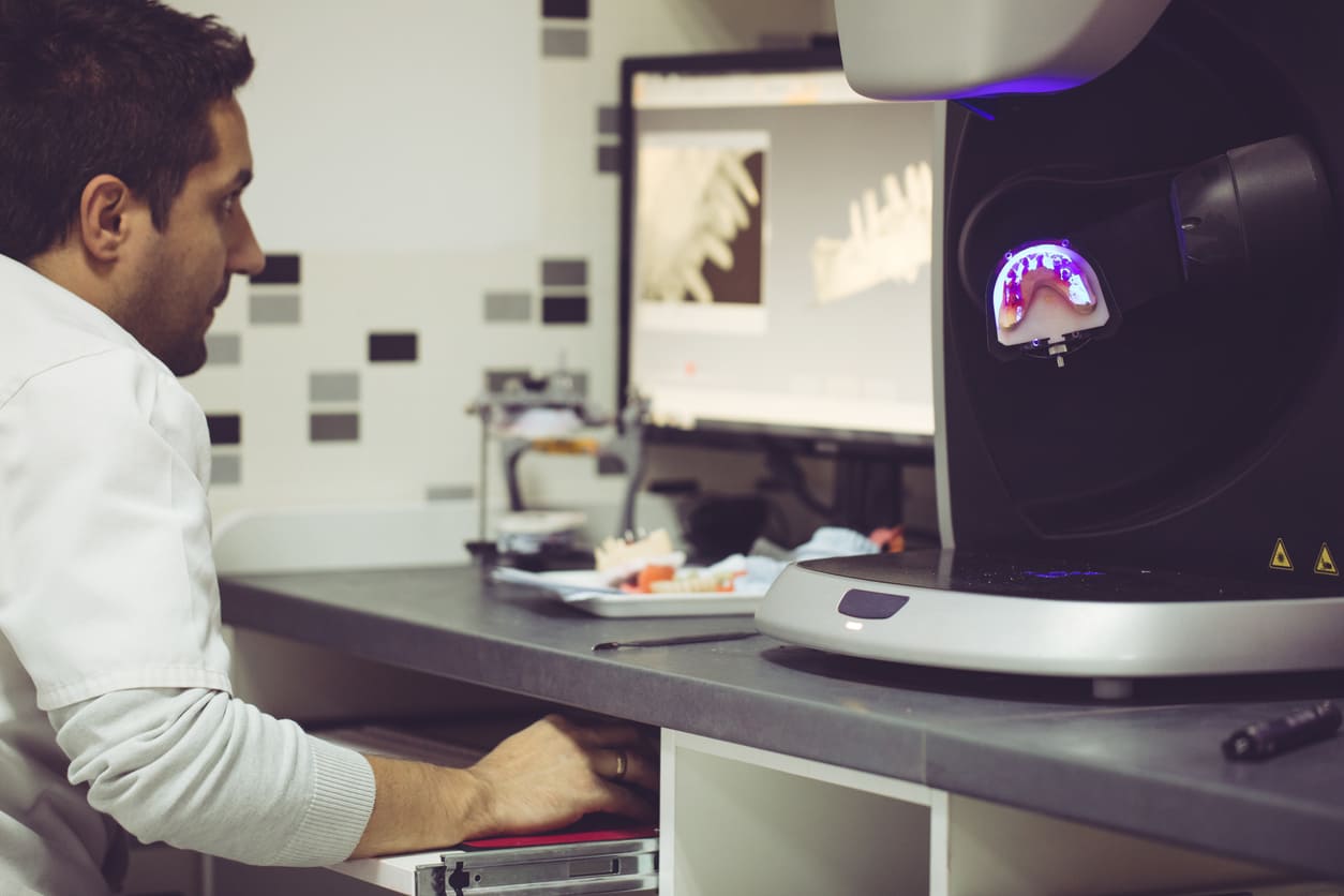 Dental technician operating 3D digital denture printing equipment with computer-designed denture model on screen