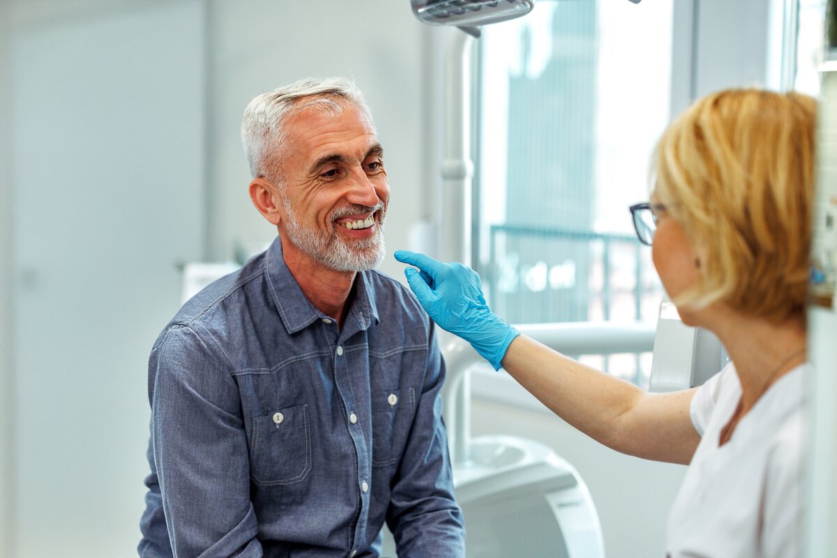 Confident senior female patient with a bright smile discussing dental care with her attentive female dentist in a warm, inviting clinic setting, reflecting positive patient experiences with Saberton dental services.