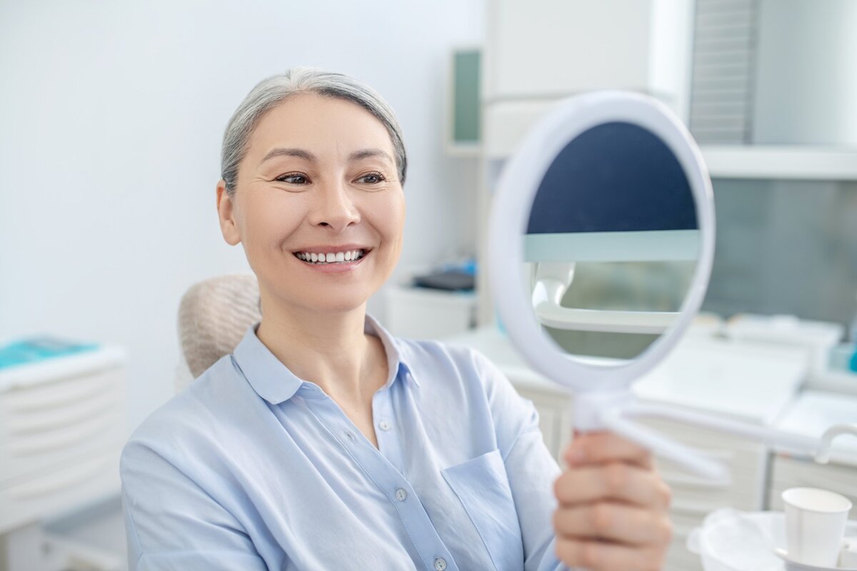 Confident senior female patient with a bright smile discussing dental care with her attentive female dentist in a warm, inviting clinic setting, reflecting positive patient experiences with Saberton dental services.