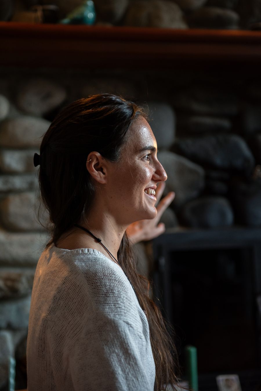 Aliya in warm profile, smiling, in front of a stone fireplace