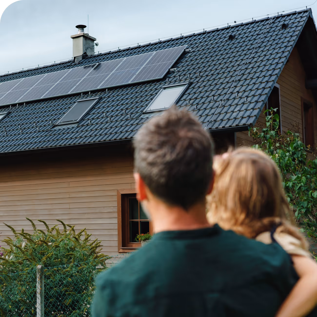 Padre con su hija en brazos de espaldas mirando a las placas solares del tejado de su casa.
