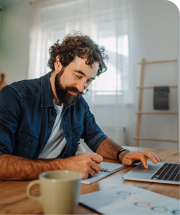 Hombre revisando su factura de la luz en el ordenador, apuntando notas en una libreta.
