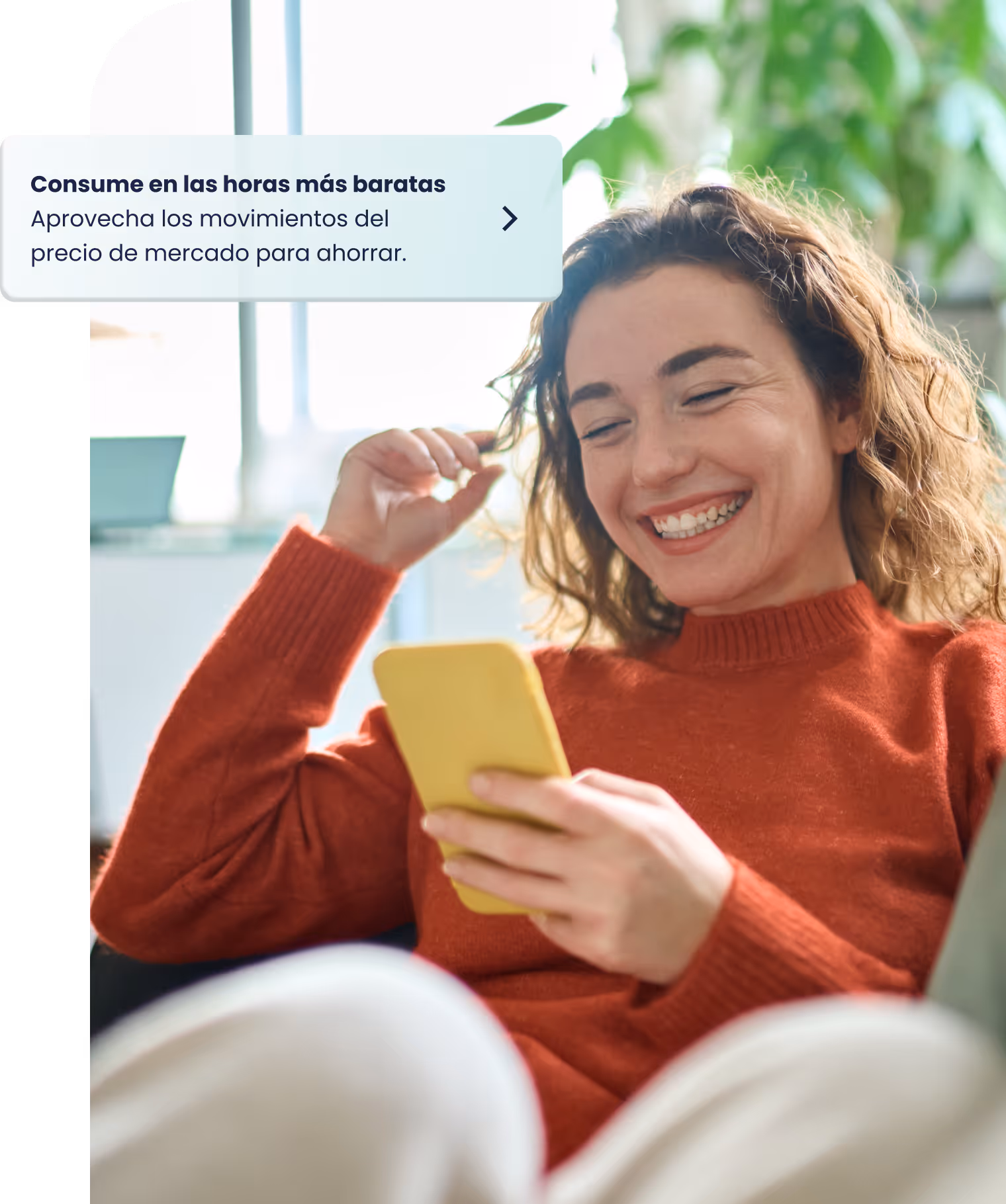 Chica joven de pelo rizado sentada en el sofá mirando su teléfono móvil.