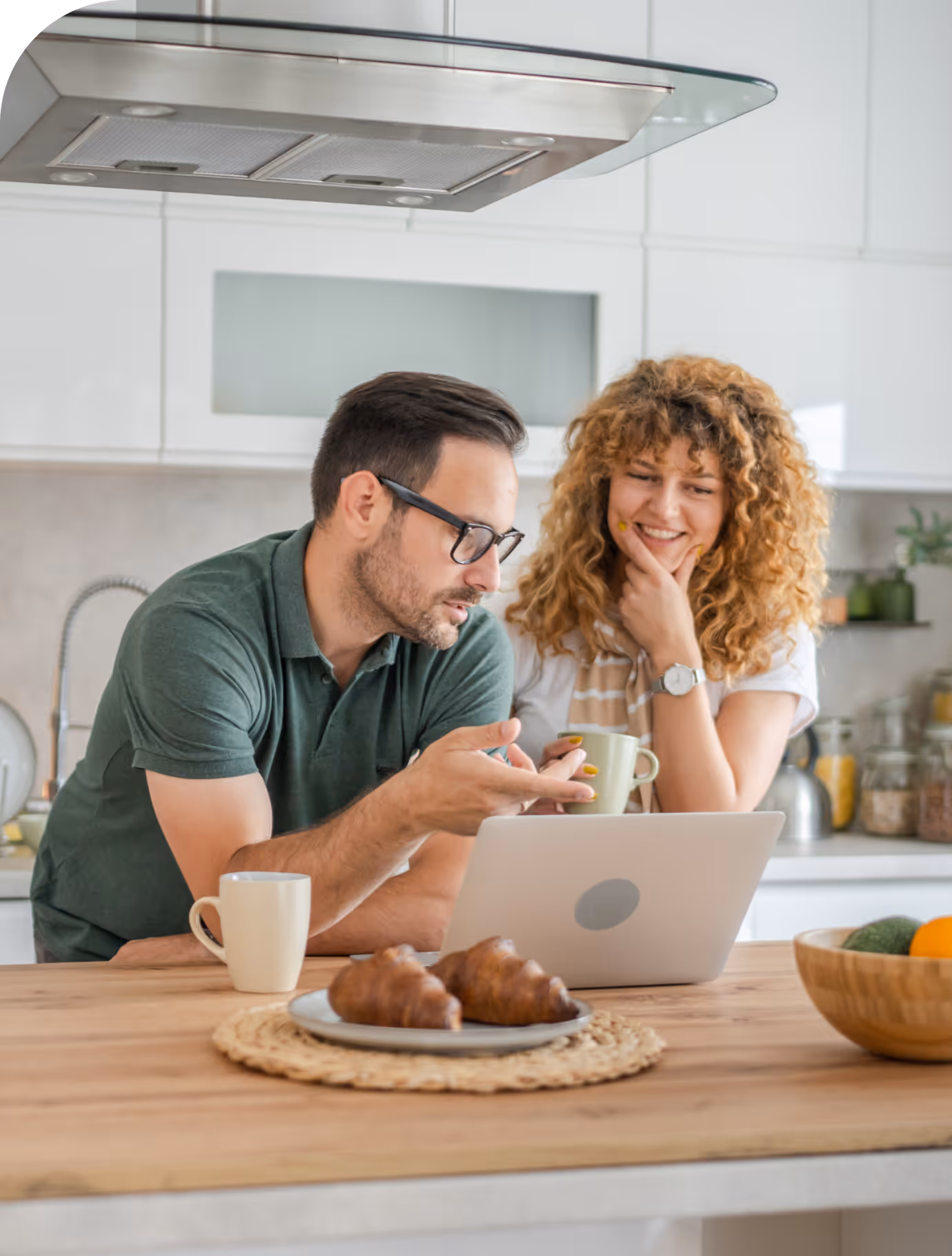Pareja mirando consultando en un ordenador portátil en la cocina de casa.