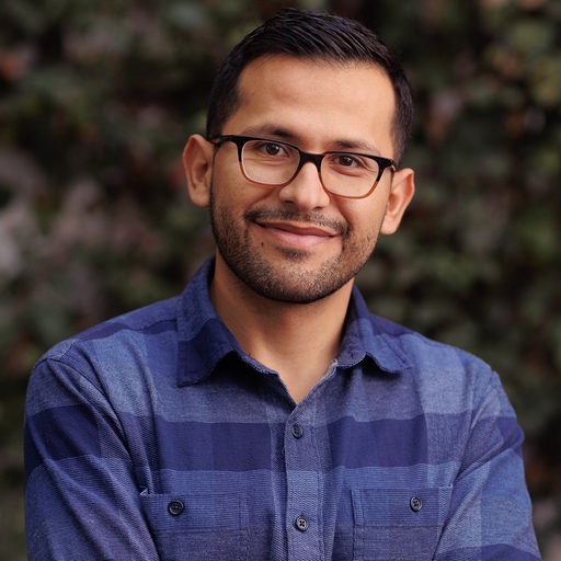A man smiling with black glasses and a blue checkered shirt