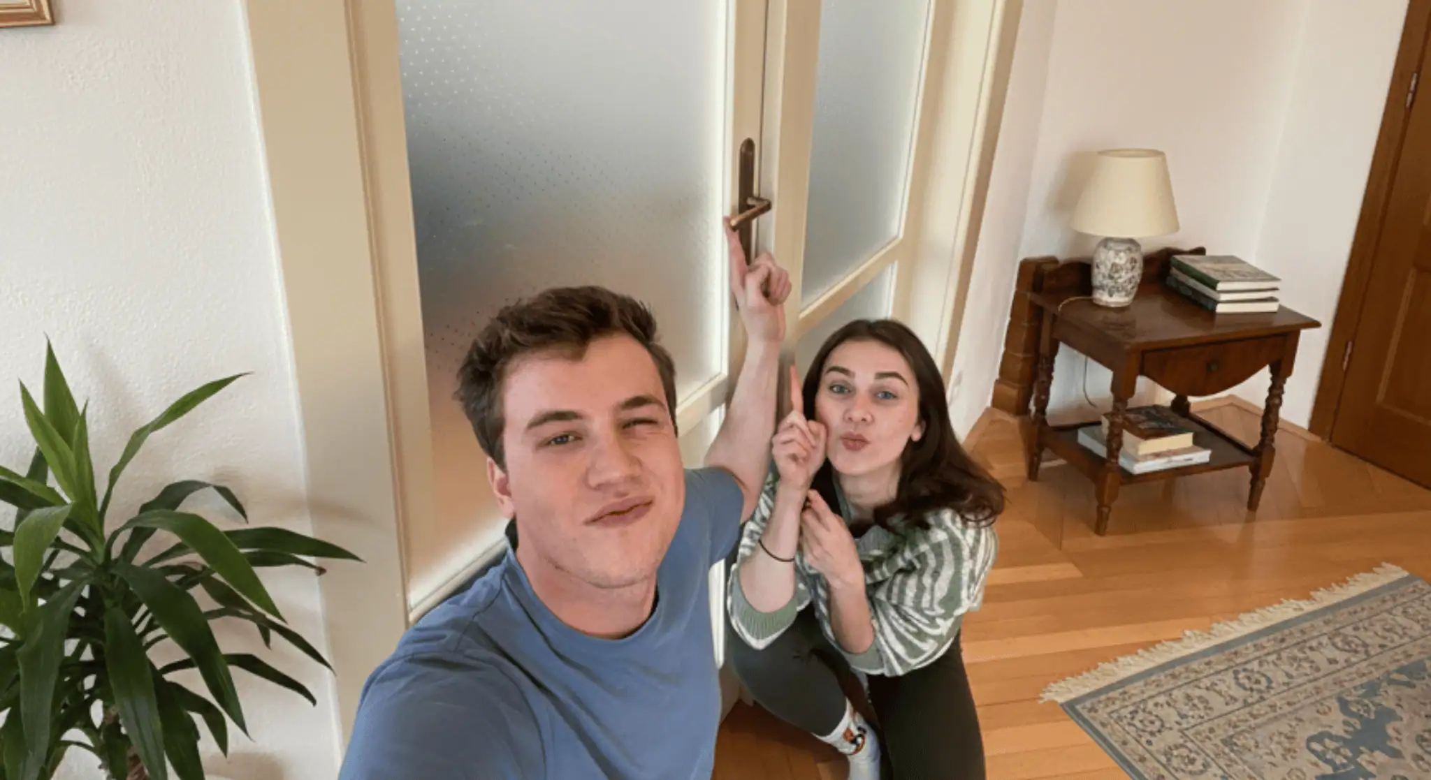 Mladý pár pózuje u dveří v novém bytě a ukazuje na kliku