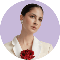 Woman with dark hair in a white blazer holding a red rose against a light purple background.