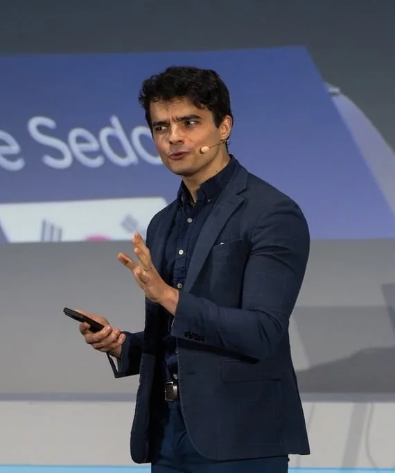 Isma Zmerli sur scène lors d’une conférence, micro-casque et télécommande en main
