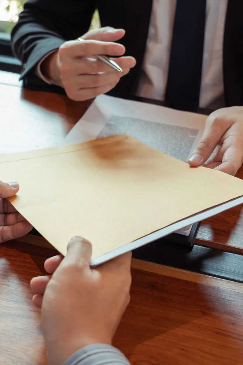 Attorney handing an envelope of legal documents to a client across a desk