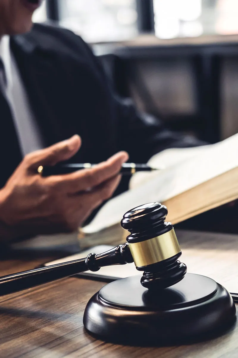 Attorney consulting an open law book at a desk, with a wooden gavel in the foreground