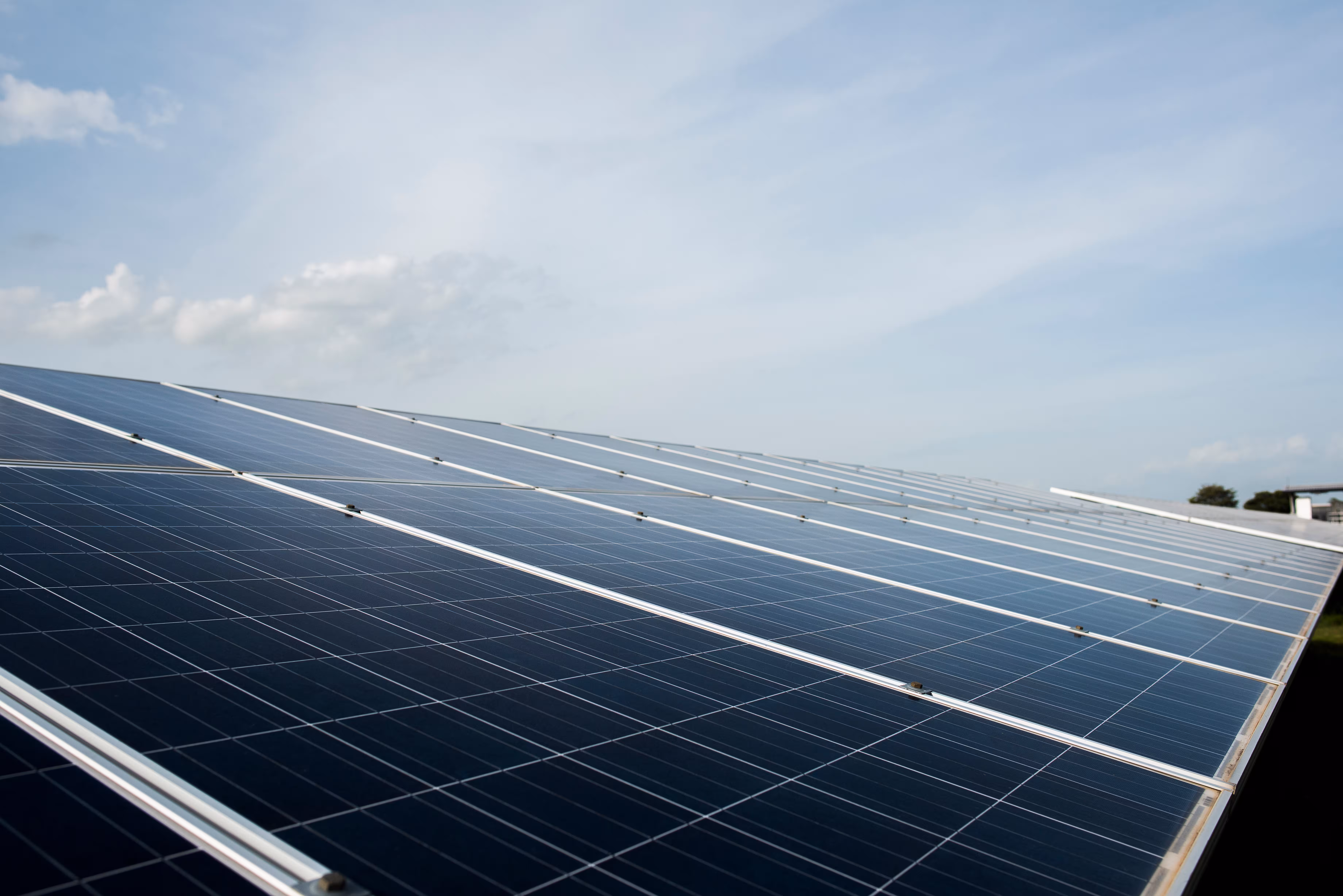 Rows of solar panels angled under a partly cloudy sky in a solar farm.