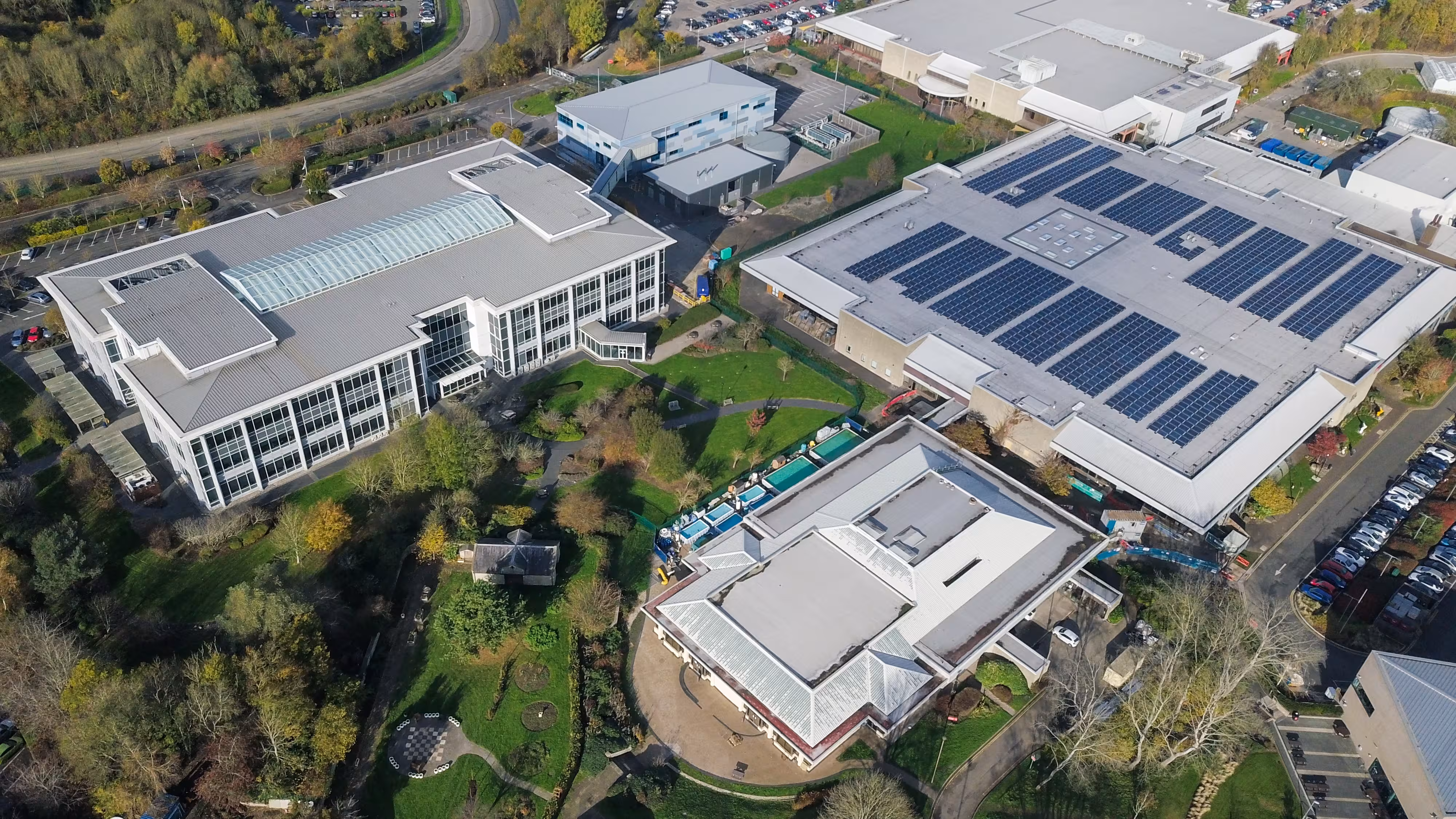 Aerial view of an industrial complex with solar panels on roofs and surrounding green spaces.