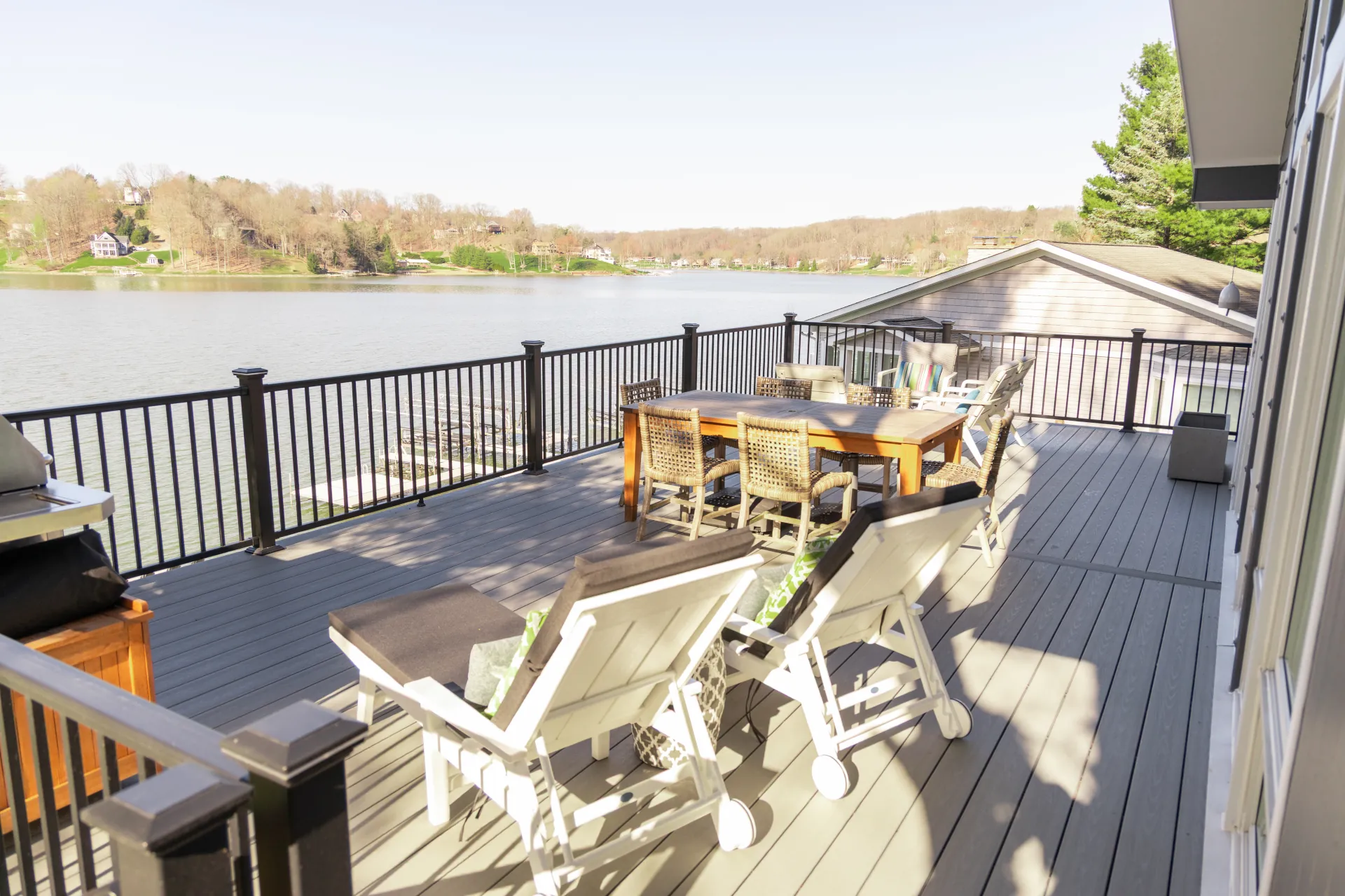 Furnished composite deck with chairs and table overlooking a calm lake and houses in the distance.