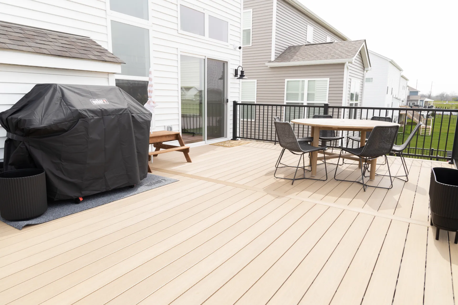 Brown composite deck with covered grill, picnic bench, round table, and black chairs in suburban backyard.