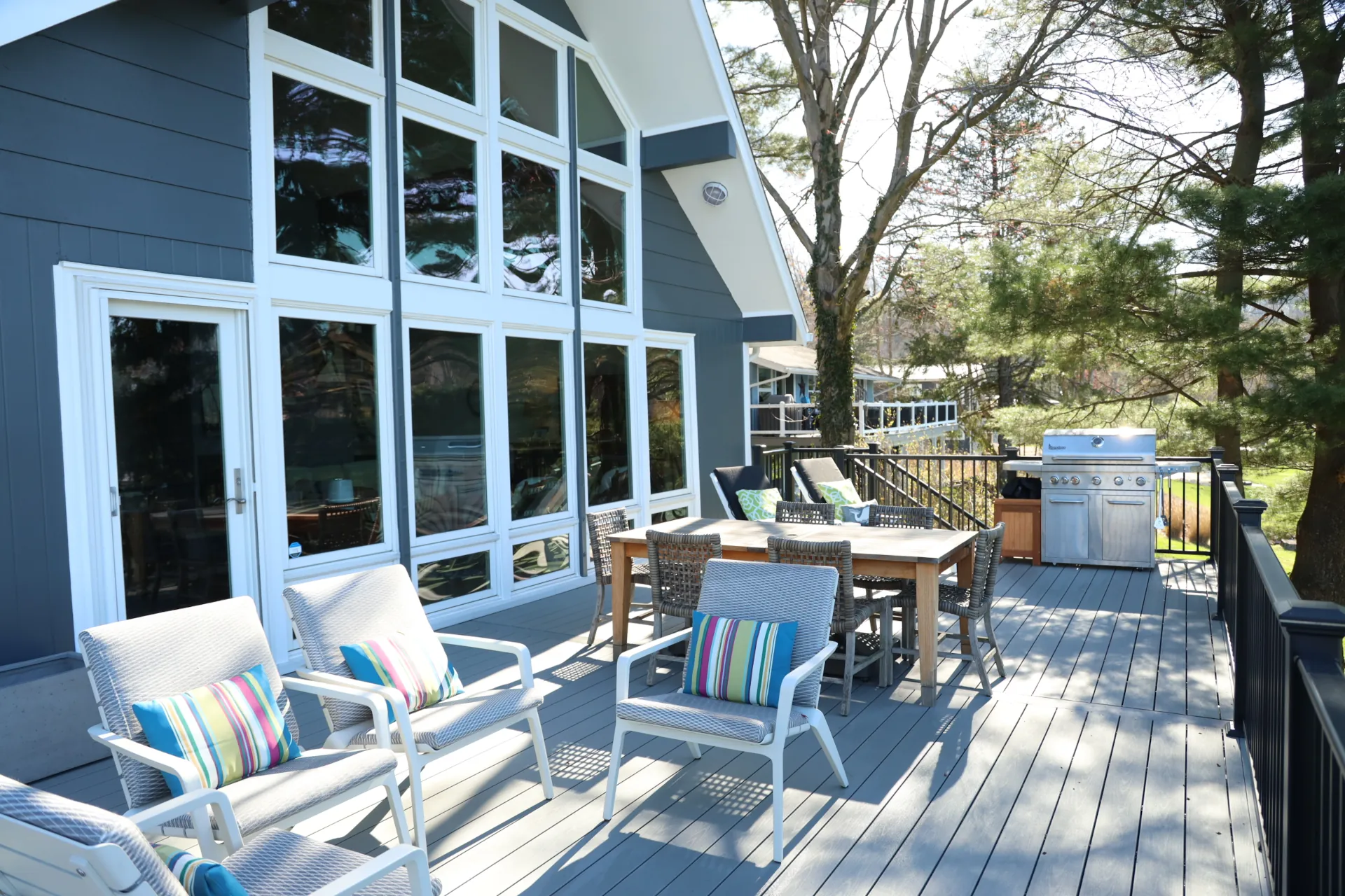 Spacious outdoor deck with chairs, dining table, and a stainless steel barbecue grill near a modern house.