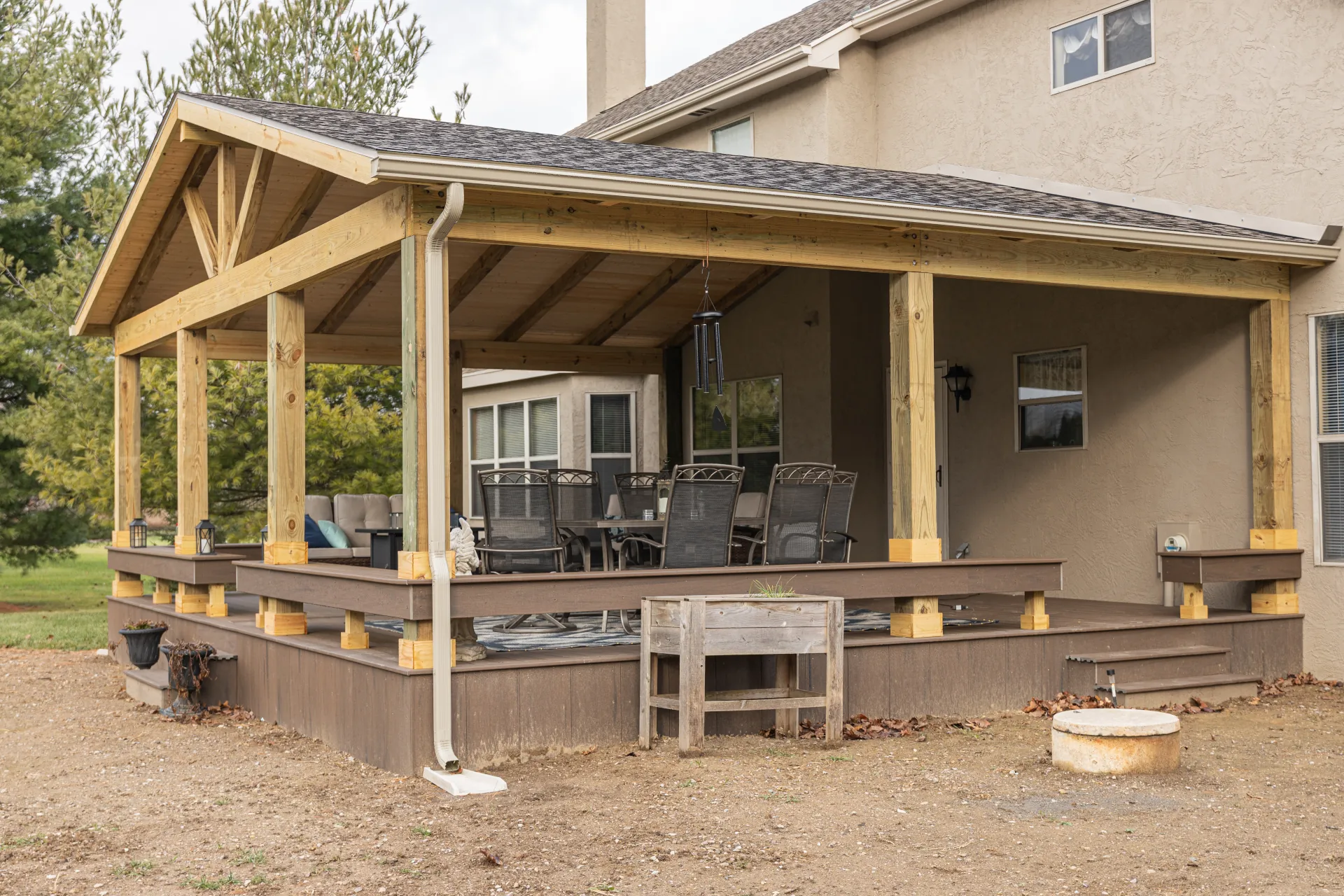 Covered wooden porch with outdoor seating and dining area attached to a beige stucco house.