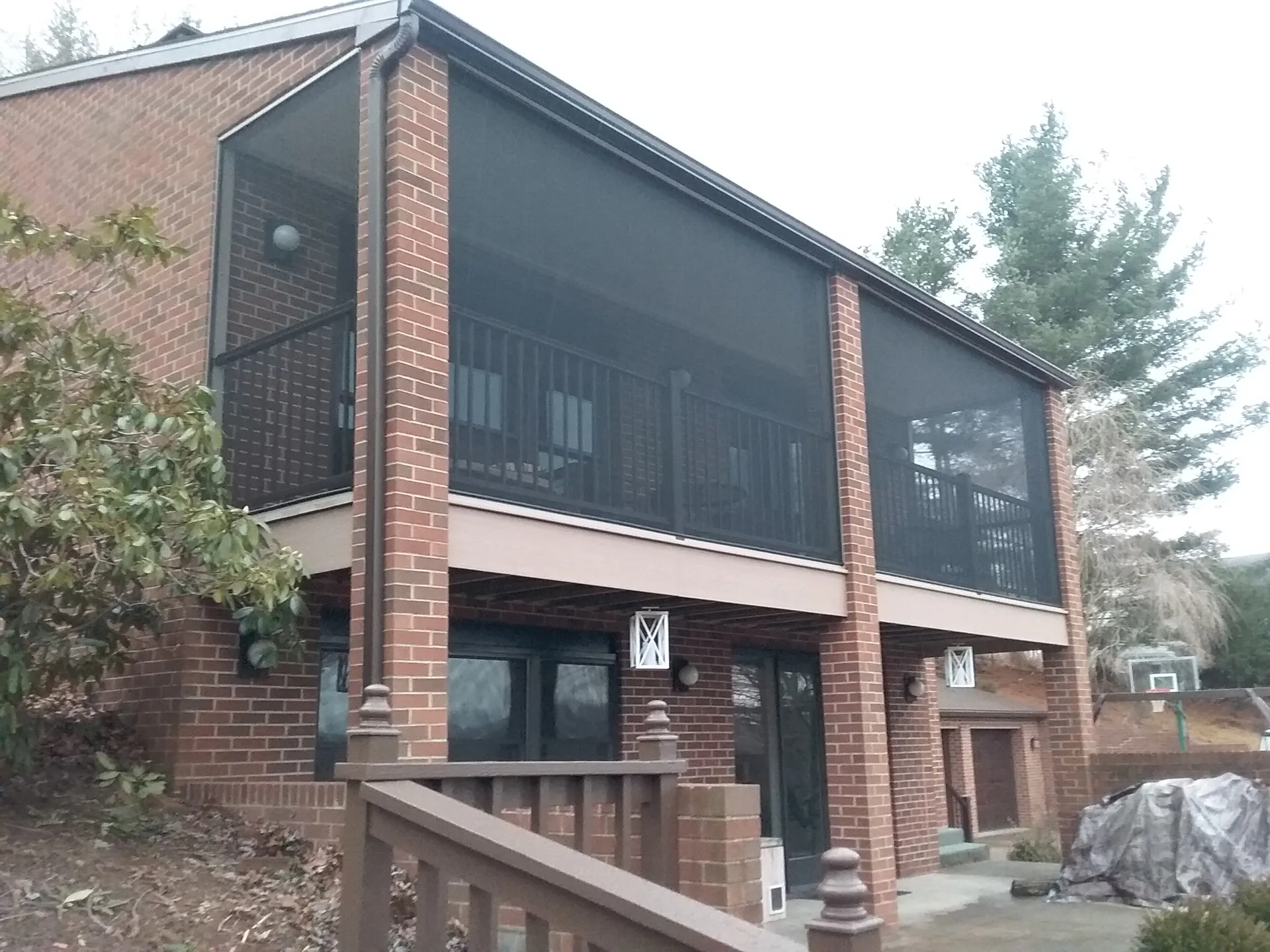 Two-story brick house with a screened porch on the upper level and patio below.