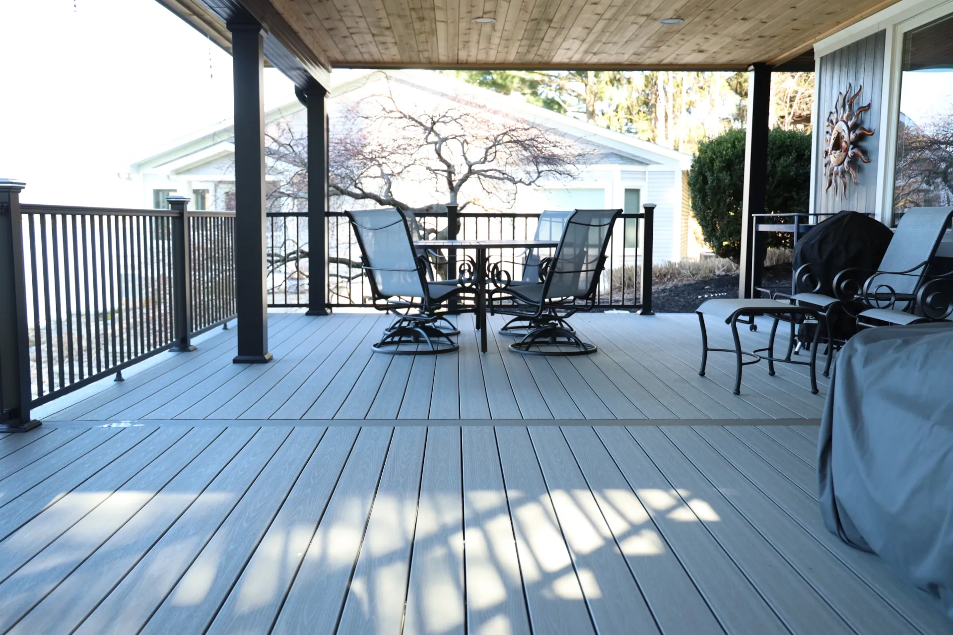 Covered grey composite deck with metal railing, four chairs around a table, and additional seating.