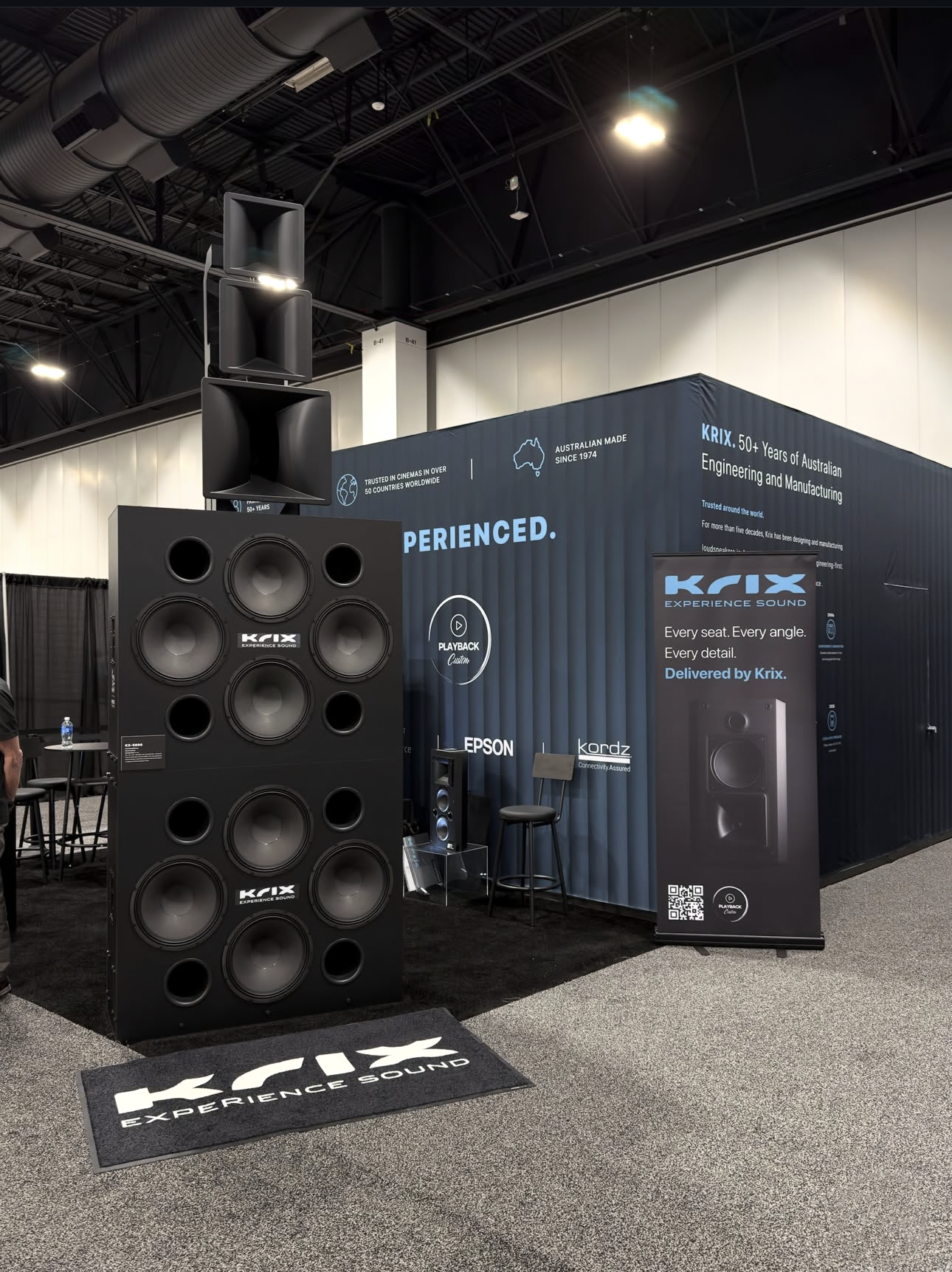 Black rectangular speaker with two large woofers, two ports, and a horn tweeter at the top.
