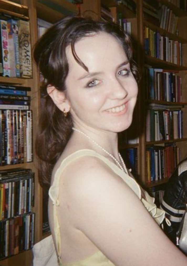 A portrait of a young woman, Jo Leuenberger, wearing a light yellow dress in a bookstore.