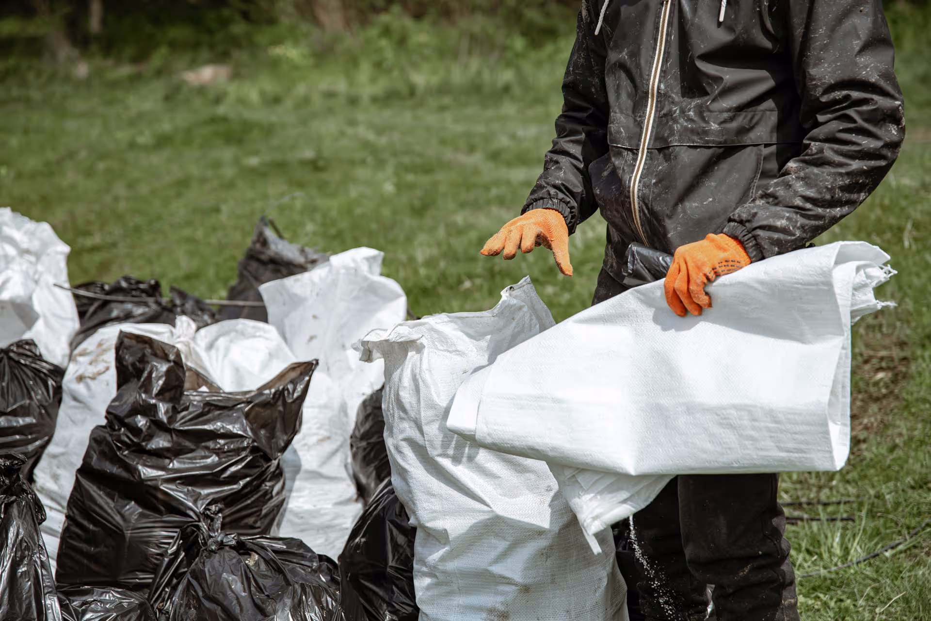 A person wearing gloves handles trash bags on grass.
