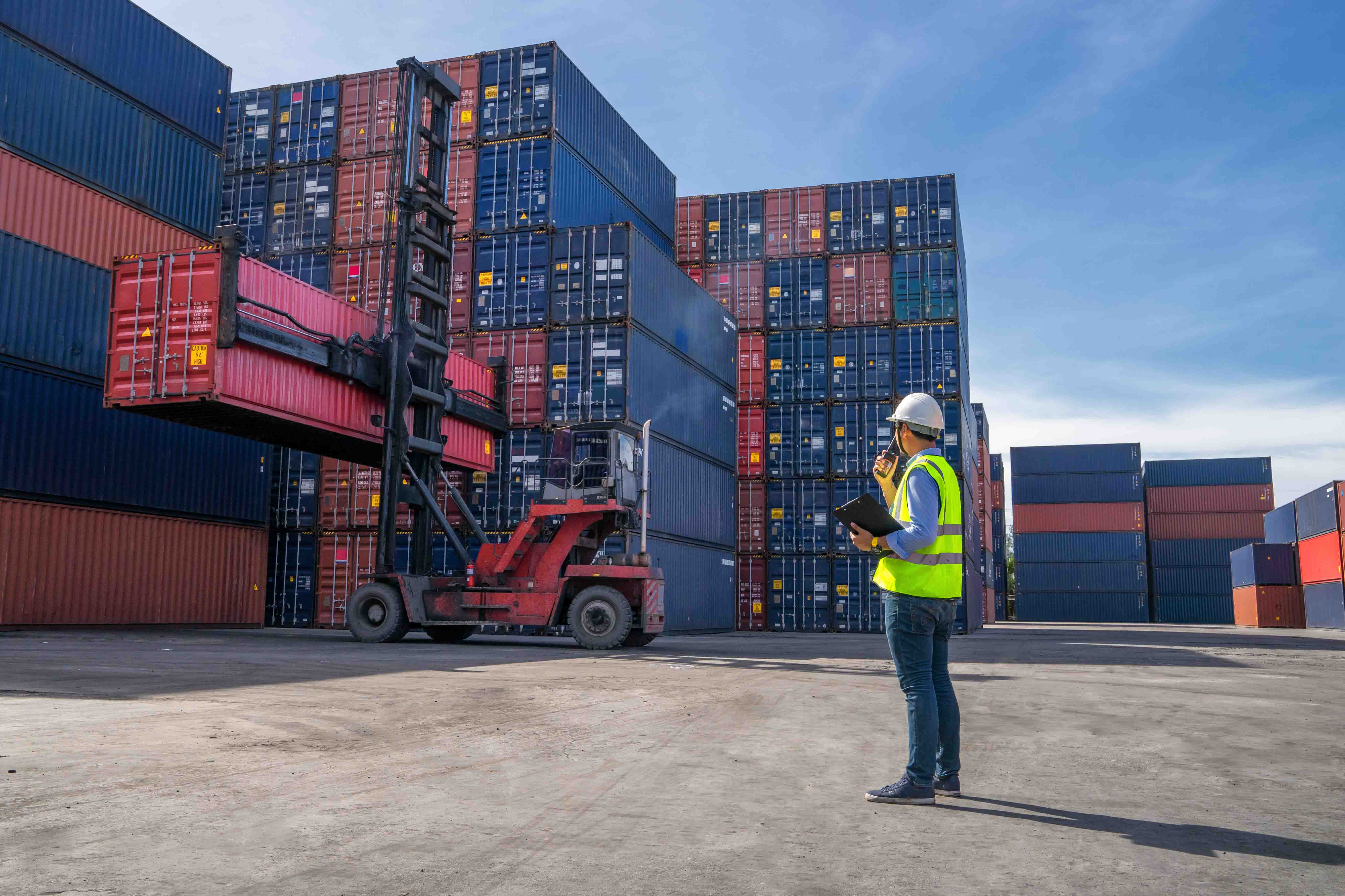Man in a high vis jacket looking up at a stack of shipping containers