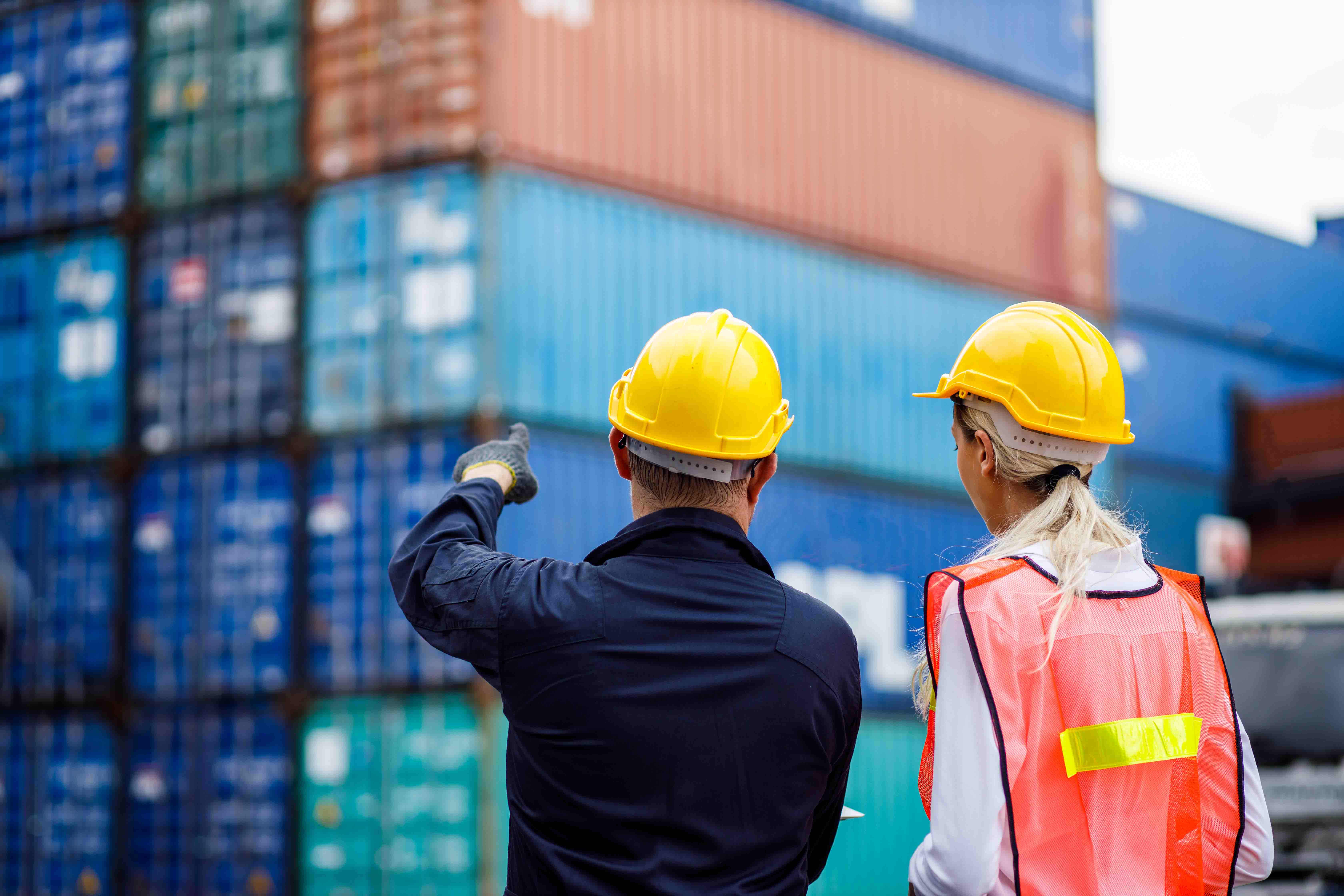 Two workman wearing yellow hardhats looking at shipping containers
