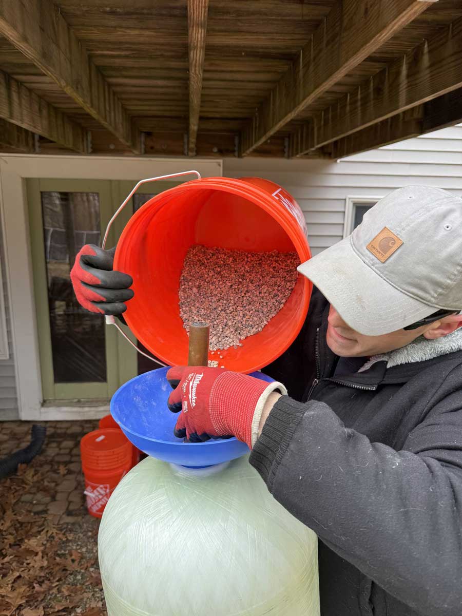 A & B Water Consultants technician loading iron filter media into a treatment tank